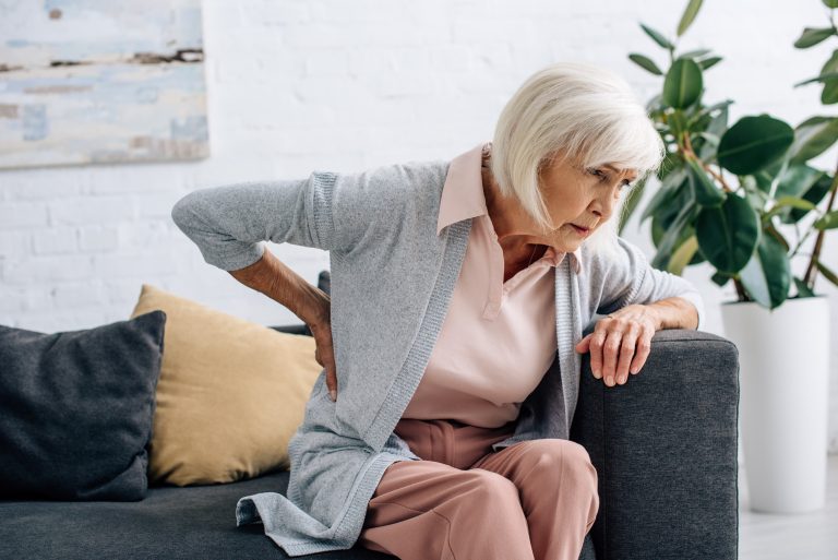 senior woman having back pain and sitting on sofa