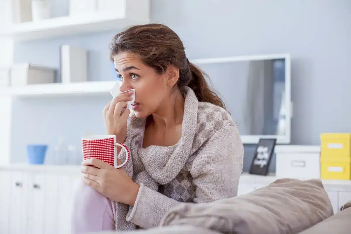woman sick ill blowing nose cold sofa